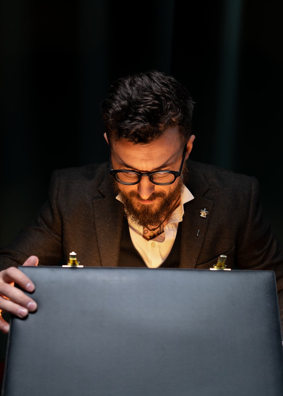 A bearded businessman in a suit intensely examines a glowing briefcase, highlighting intrigue.